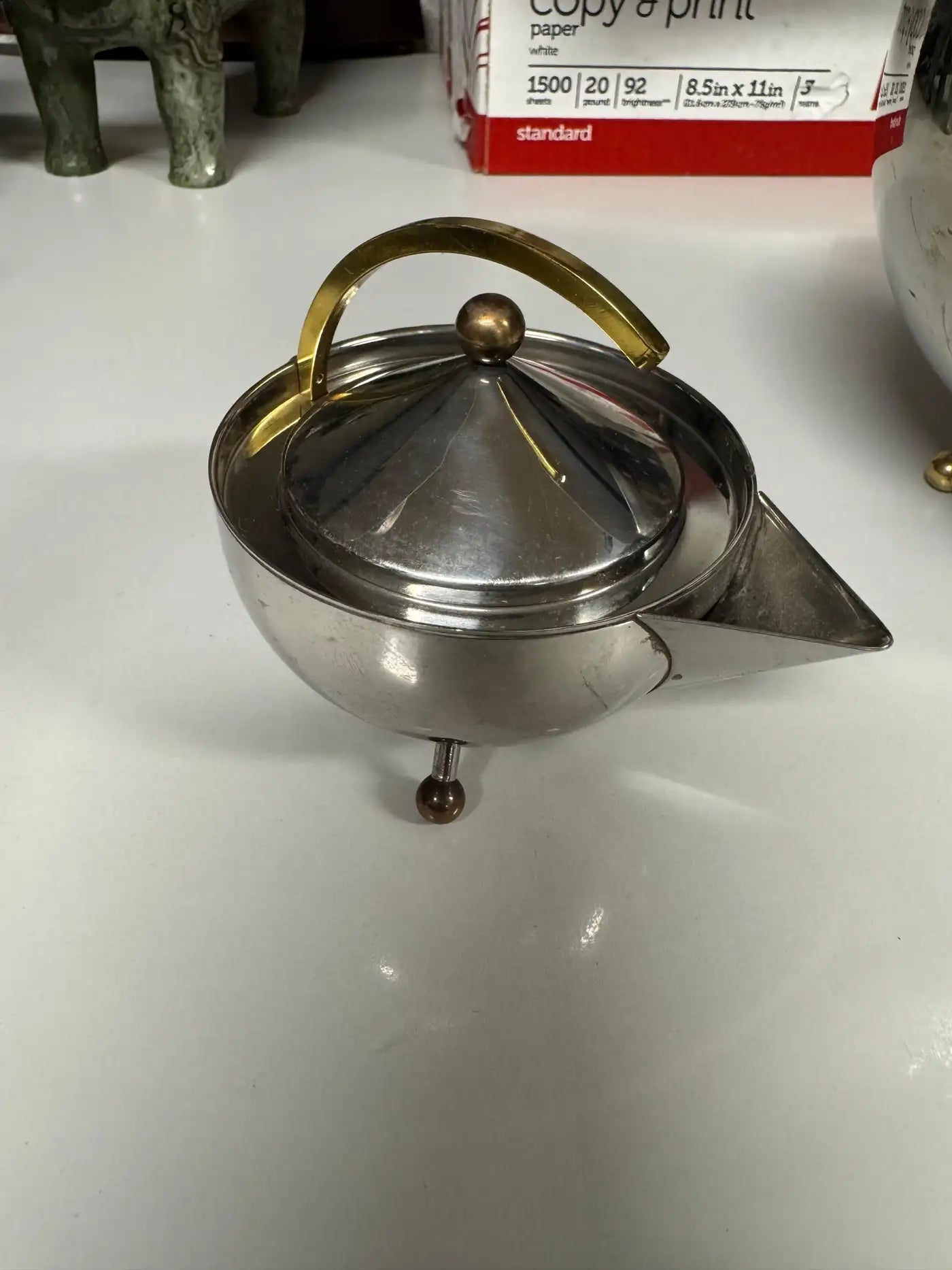Close-up of polished stainless steel surface and brass accents on Carsten Jorgensen for Bodum ball teapot.