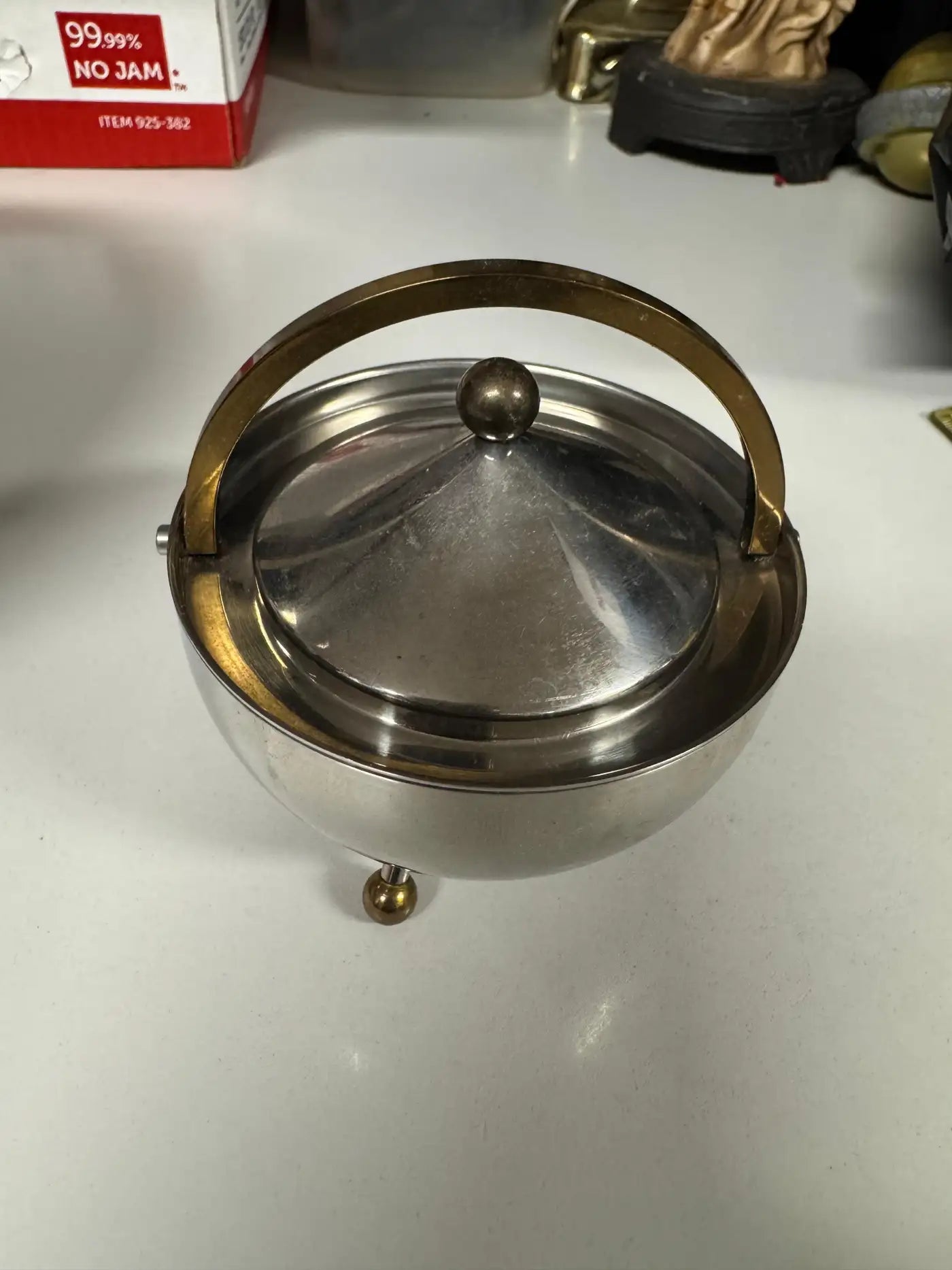 Rounded stainless steel sugar bowl with arched brass handle and tripod feet from vintage Bodum tea set.