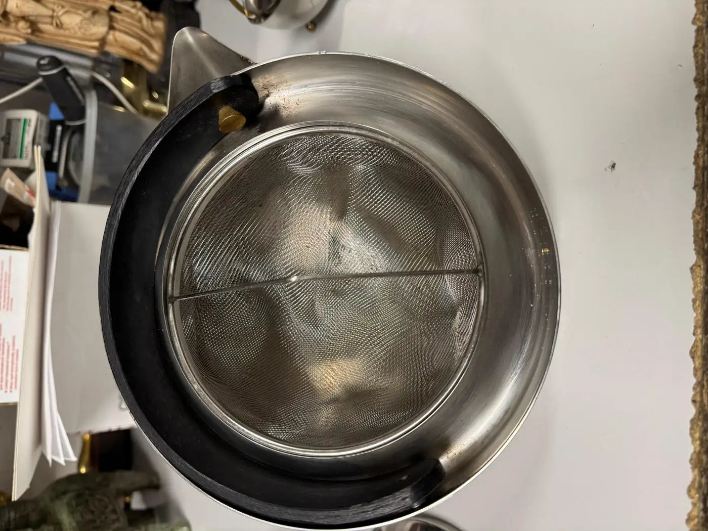 Top angle of polished stainless steel Bodum tea pot showing conical lid, brass knob, and dramatic rounded bowl body